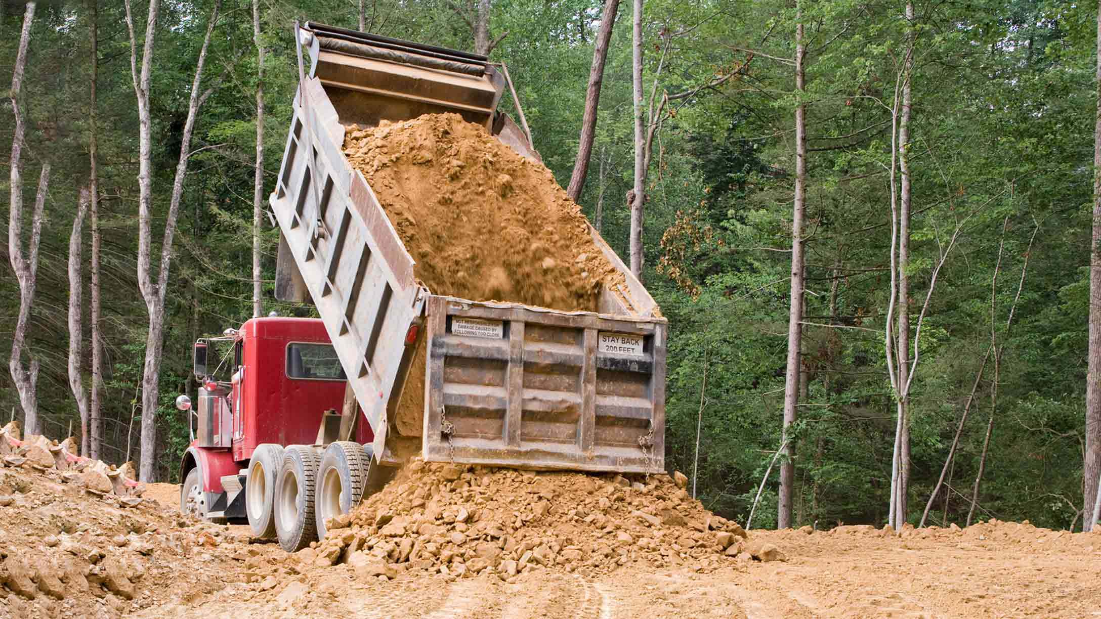 Dump truck dumping soil near a forest