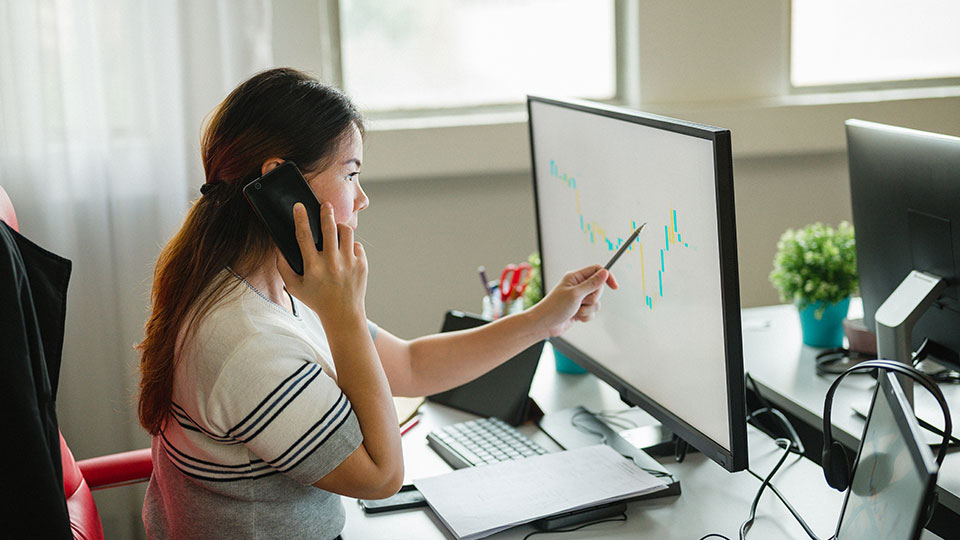 Foto de una mujer hablando por teléfono frente una computadora.