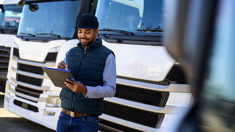 Worker standing and looking at clipboard in front of parked trucks