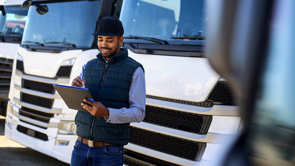 Mann vor einem LKW mit Tablet in der Hand. 