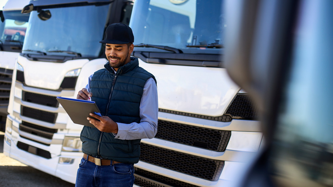 Worker standing and looking at clipboard in front of parked trucks