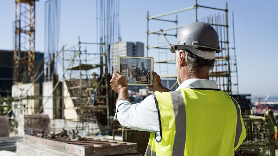 A man at a construction site looking at a tablet screen 