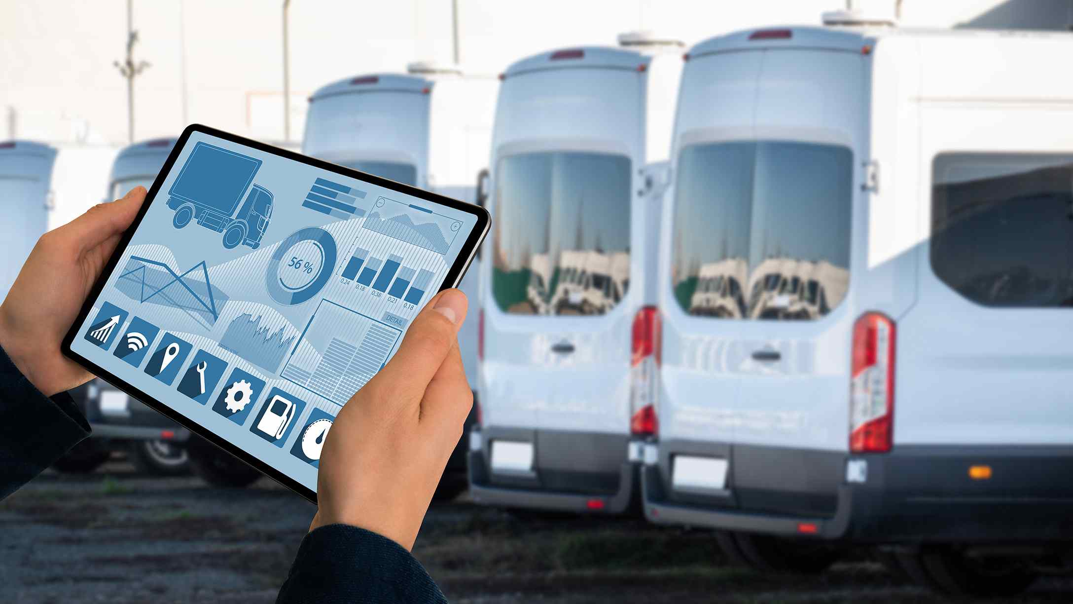 Imagen de persona viendo un tablero estratégico en tableta electrónica, detrás de una fila de camionetas blancas