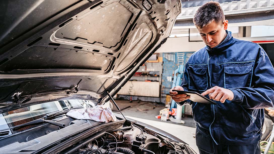 A mechanic looking at tablet computer near a car engine. 