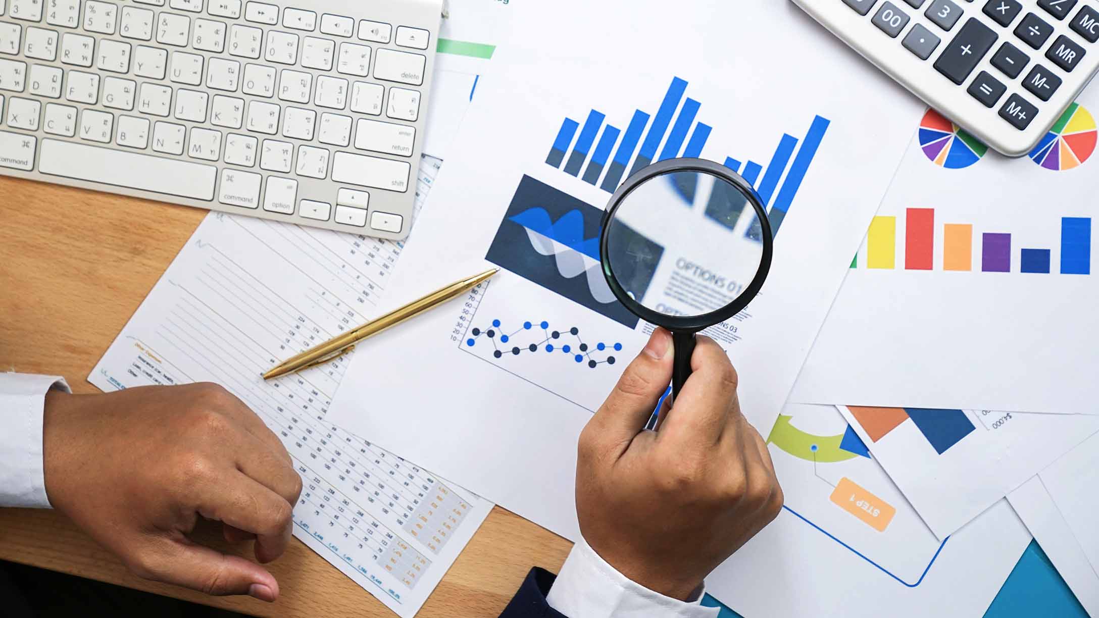 A hand looking at data under a magnifying glass. 