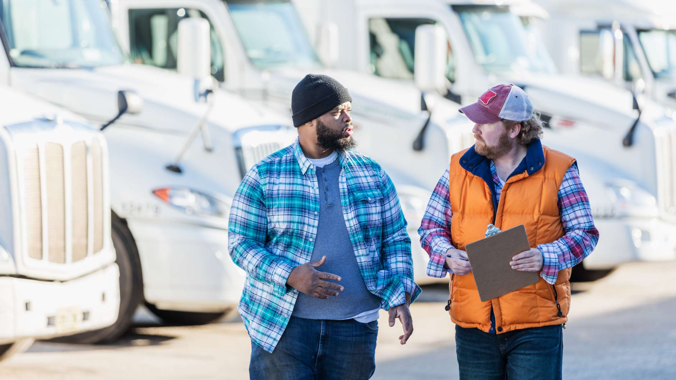 Two people standing in the foreground of a fleet of trucks