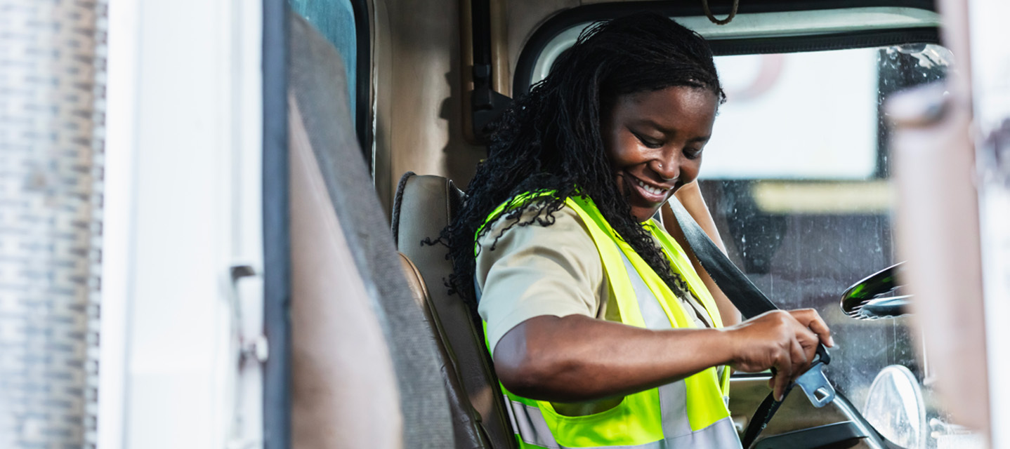 A woman in a safety vest sitting in a fleet car about to buckle her seatbelt.