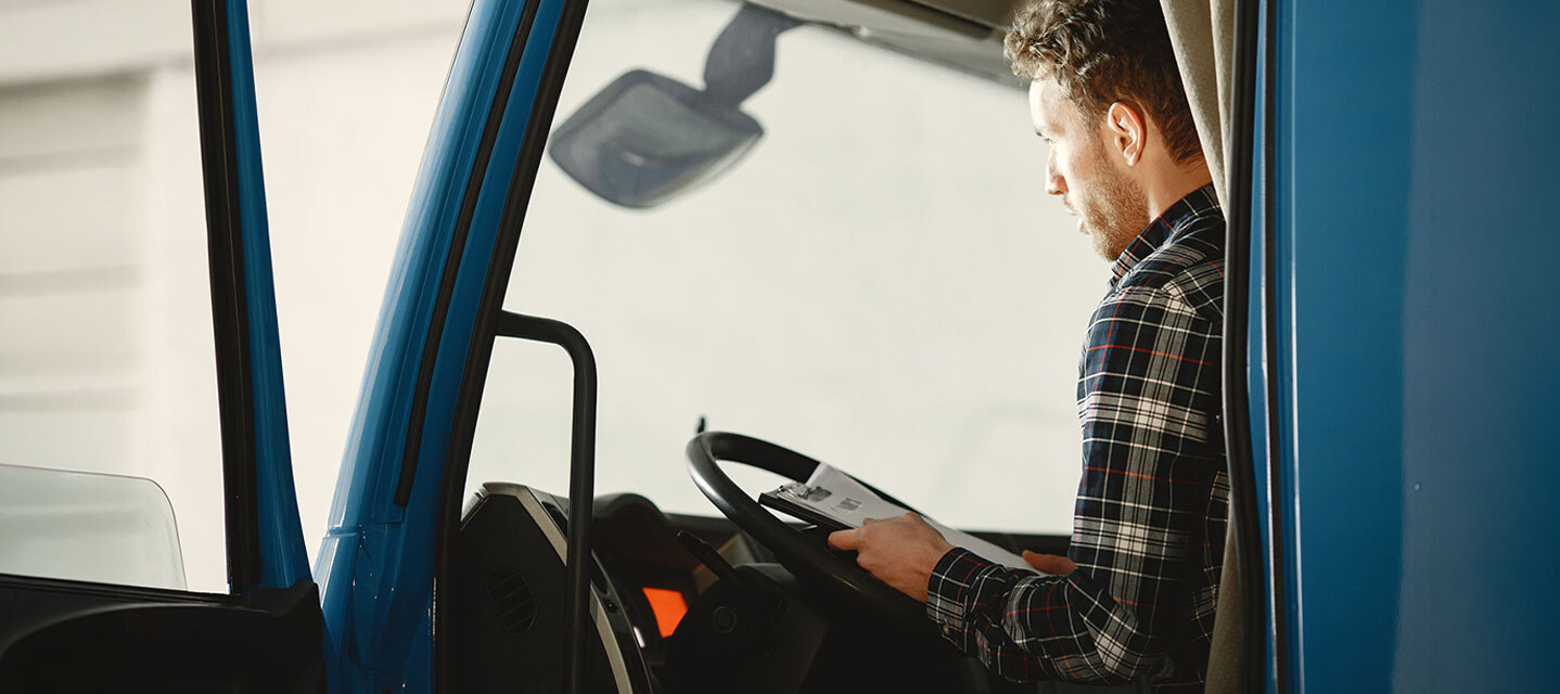 A man in a plaid shirt sitting in the driver's seat of a blue fleet truck with the door open.