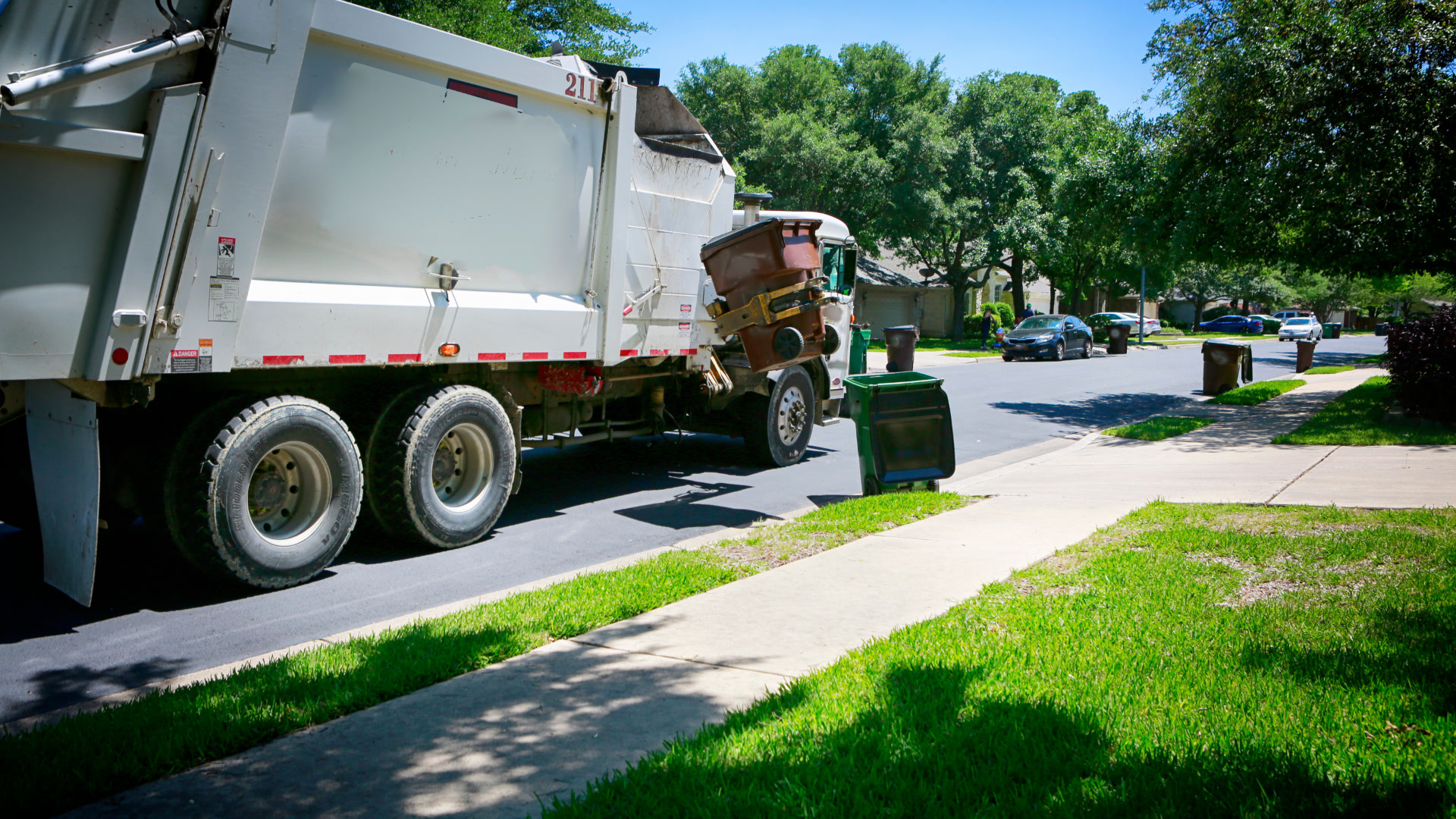 Garbage truck collecting waste bins on a residential street.