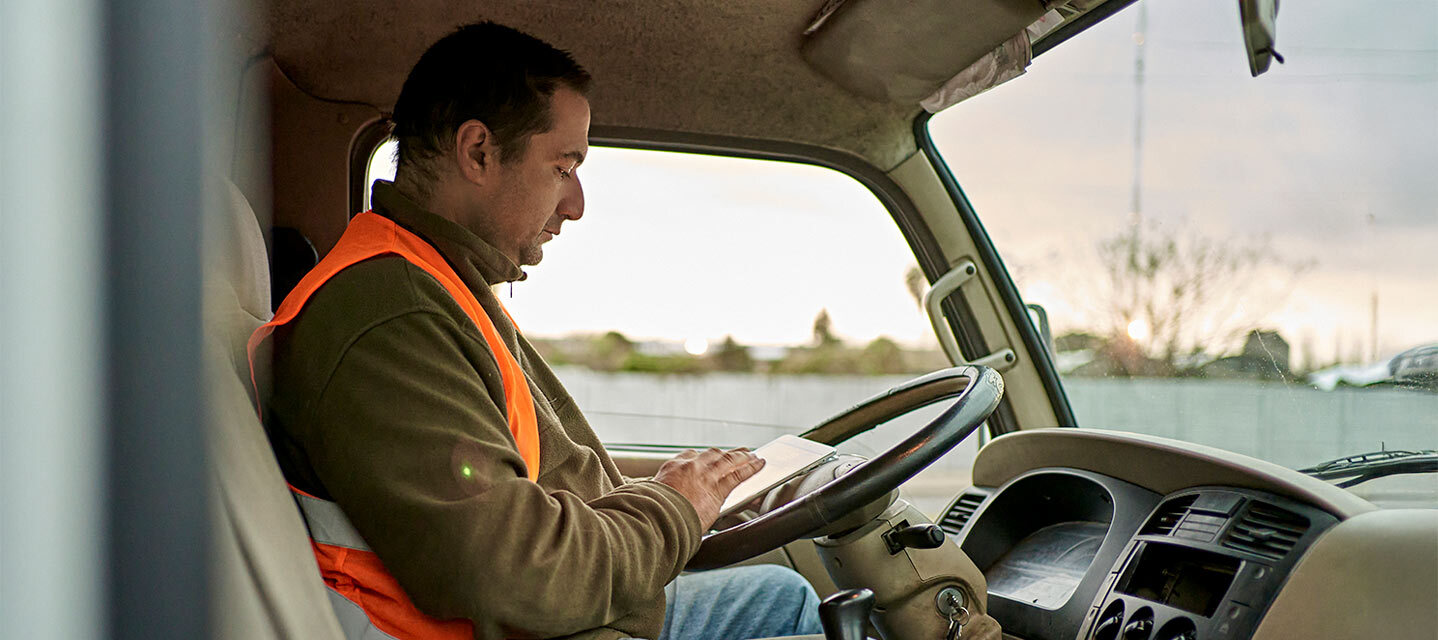 A fleet driver sitting in the passenger seat looking down at a tablet. 