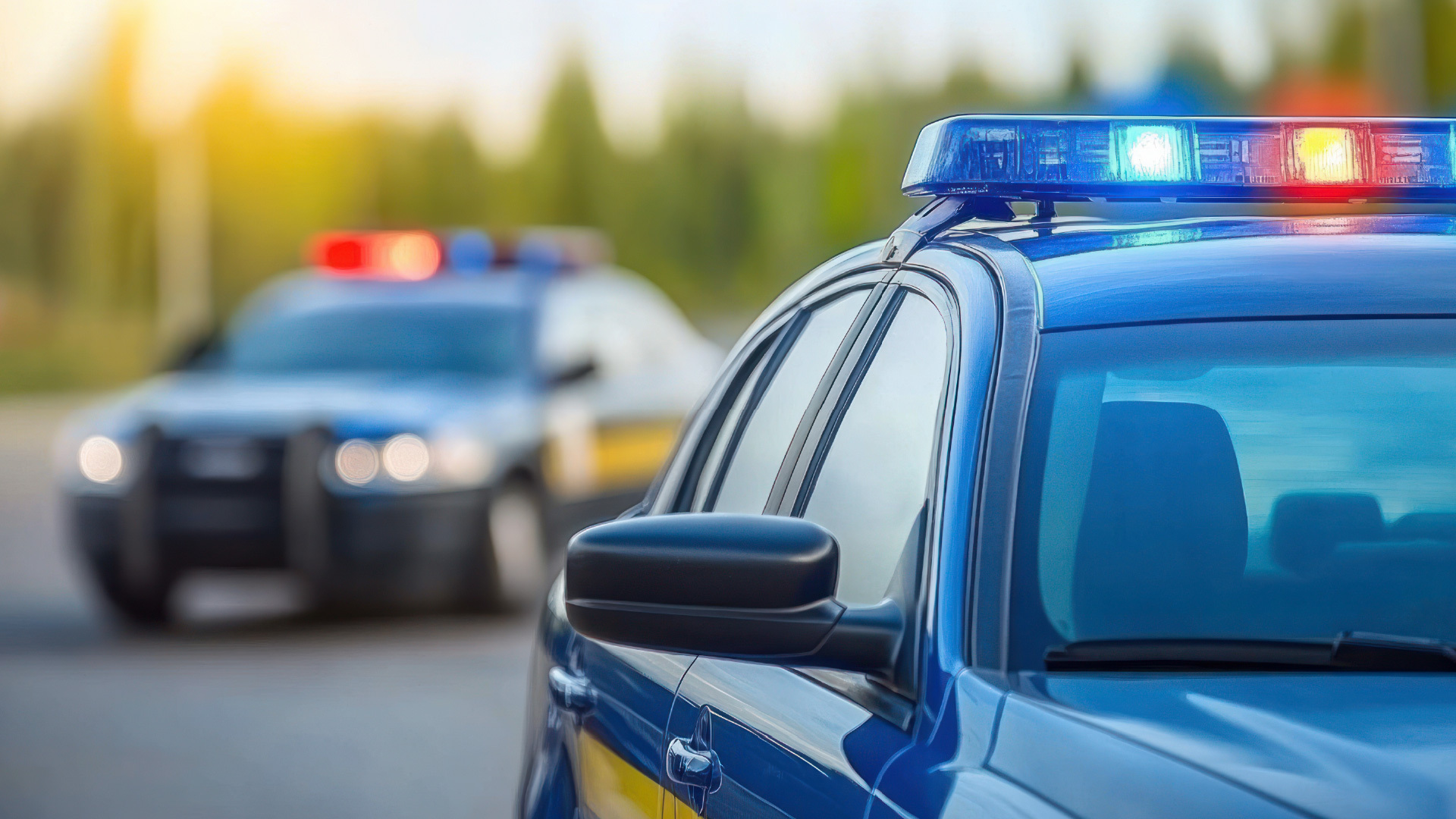 Close-up of a police car with activated lights and sirens, with additional patrol vehicles blurred in the background on a highway