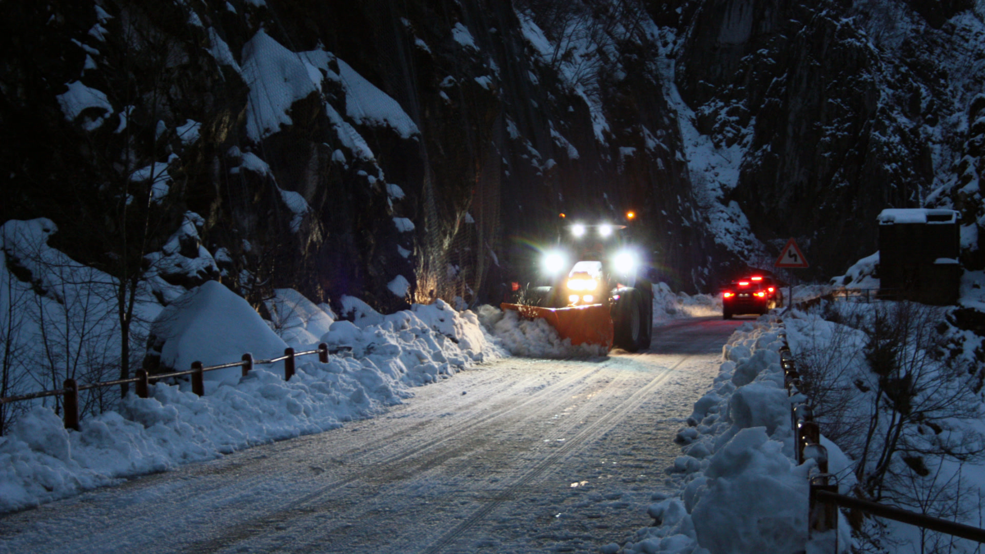 Snow plow clearing a snowy mountain road at night