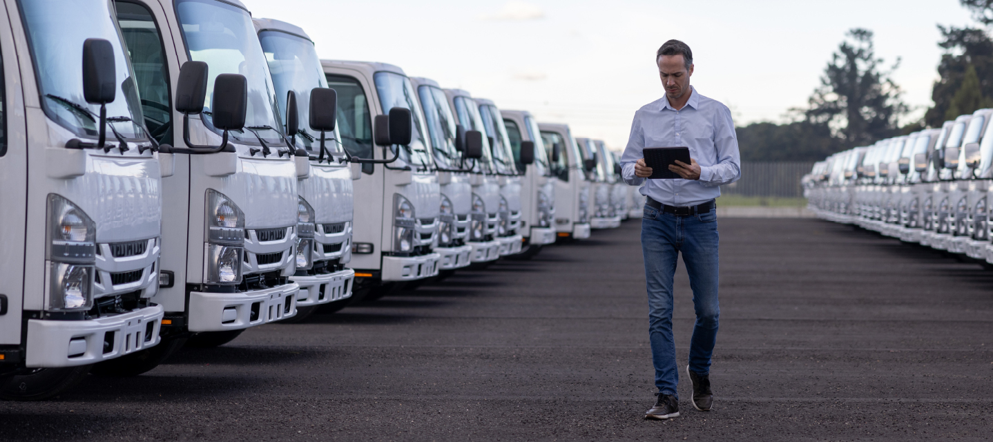 A man with a table walking through a row of white fleet trucks outside. 