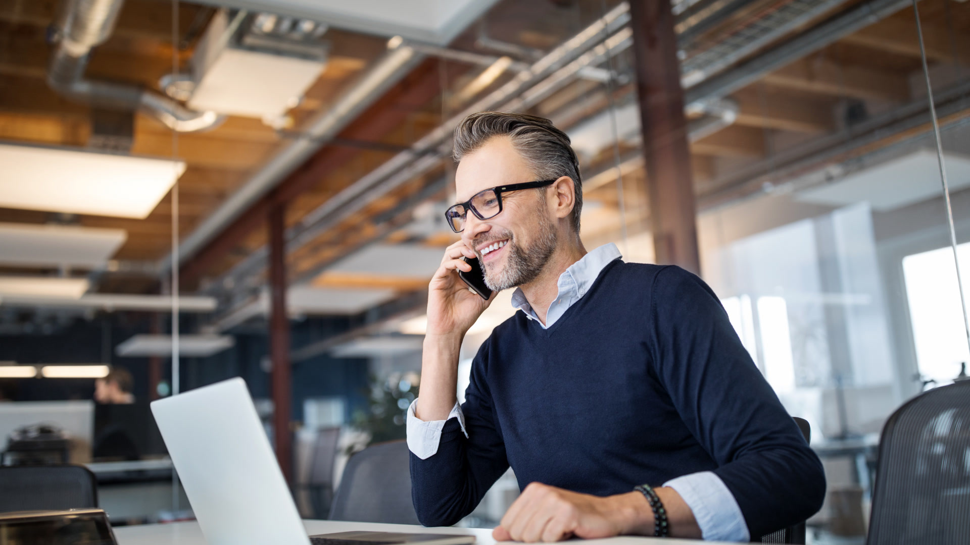 Smiling public sector fleet manager on a phone call while reviewing driver risk management data on a laptop in an office.
