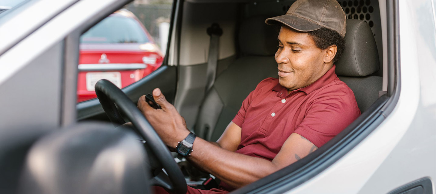 A man in the driver's seat of a fleet vehicle looking at a phone.