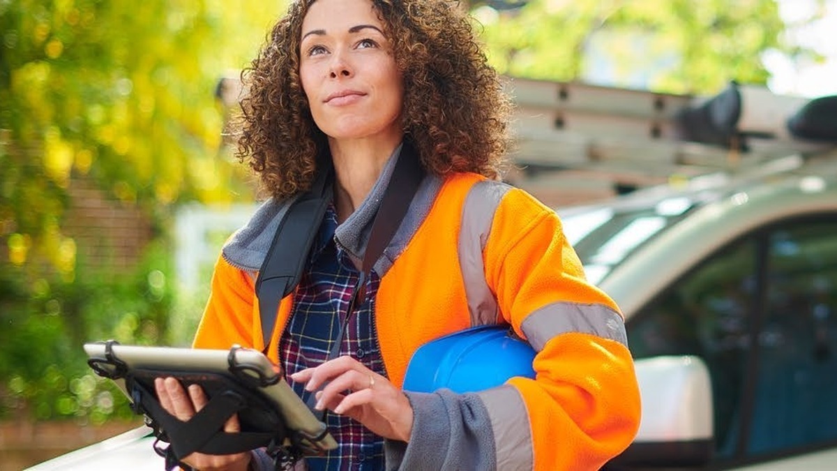 Utility technician in a high-visibility jacket holding a tablet beside a service van at a remote work site