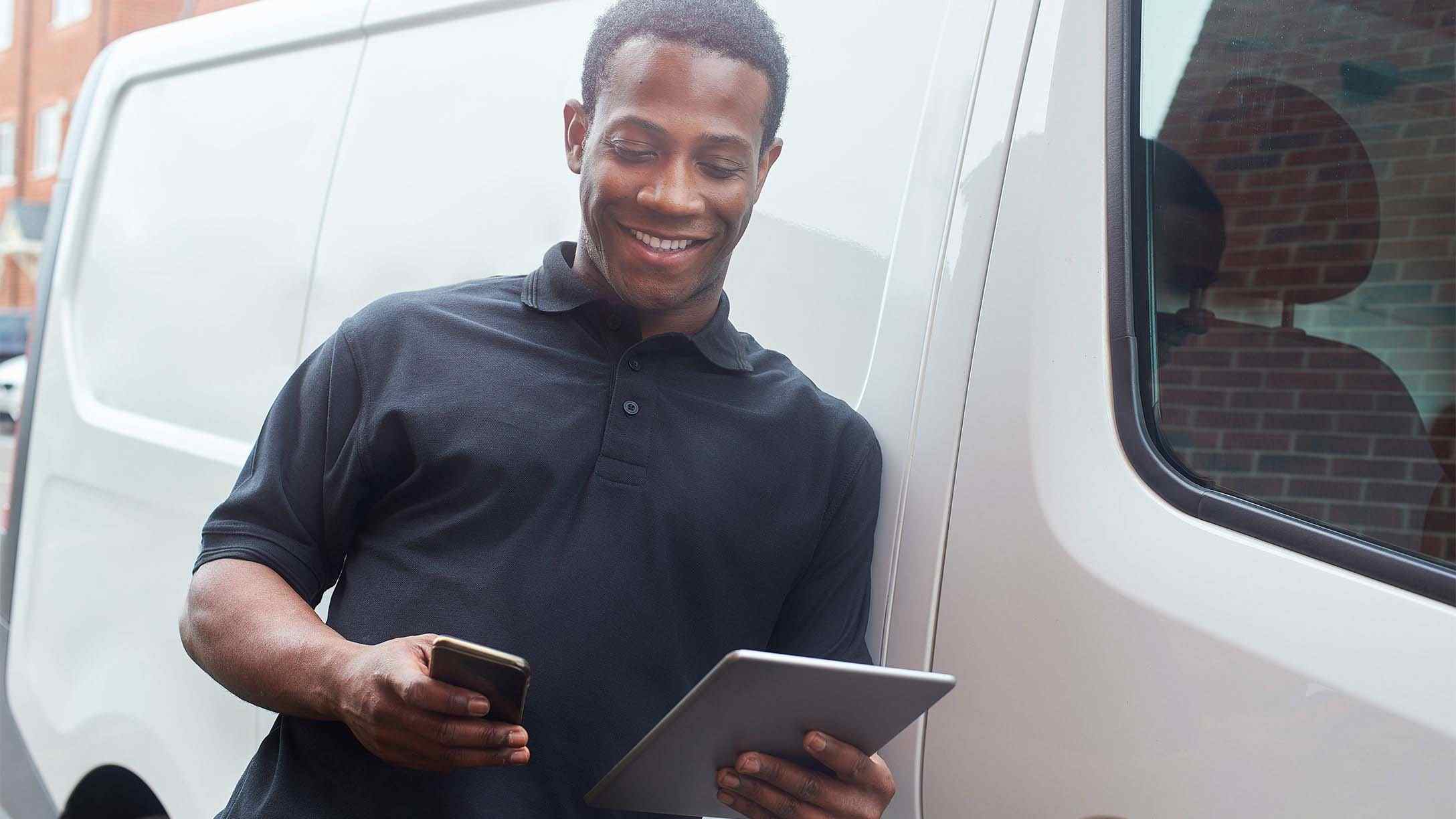 Person leaning against a vehicle looking at a tablet and phone