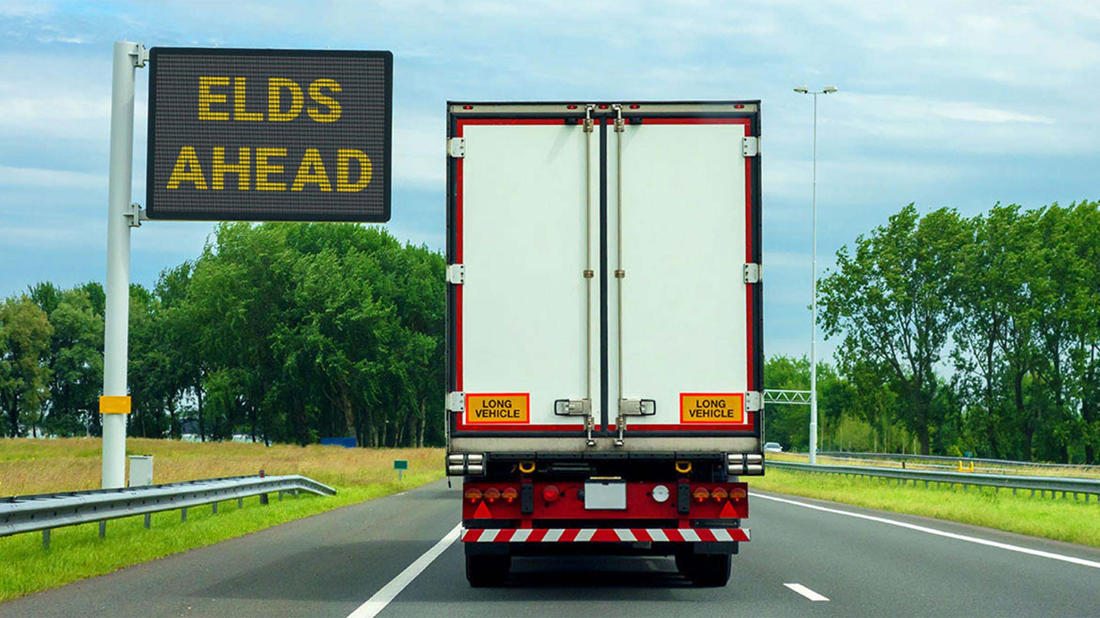Back of a white transport truck on a road with a road sign saying "ELDS AHEAD"