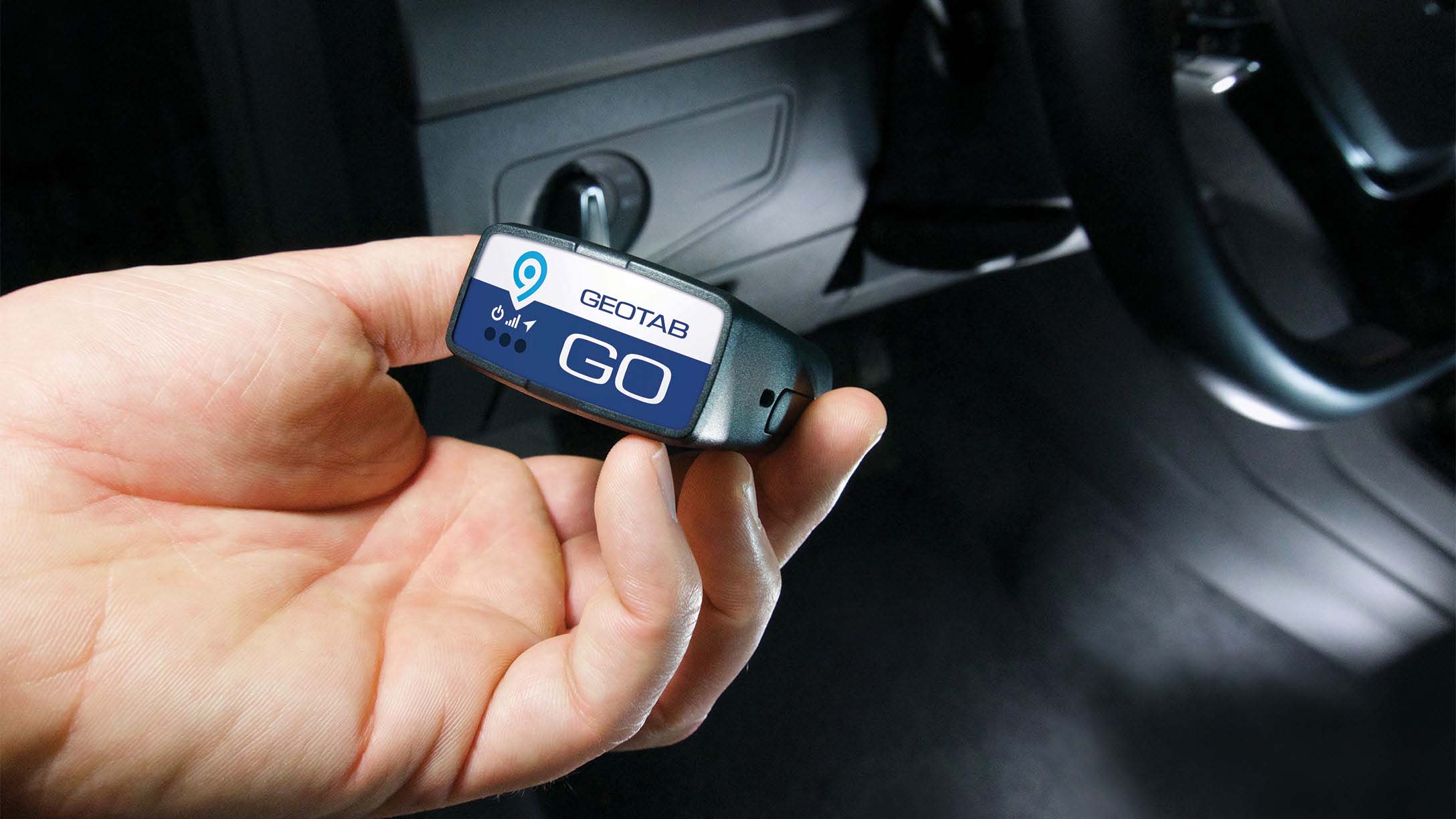 Hand holding Geotab GO device with vehicle dashboard in the background