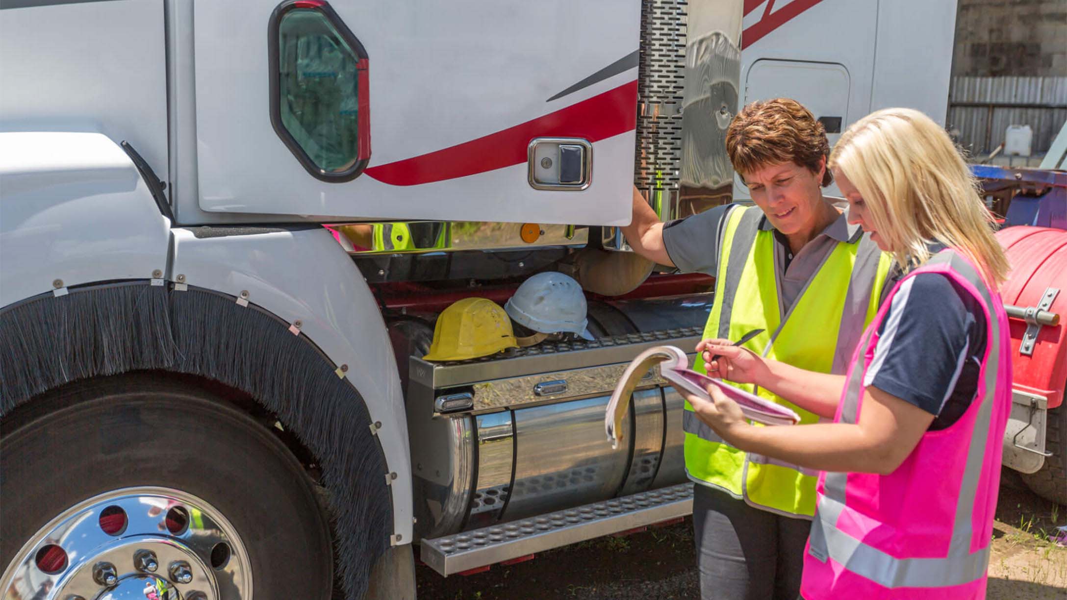 Two women standing outside a semi truck looking at a clipboard 