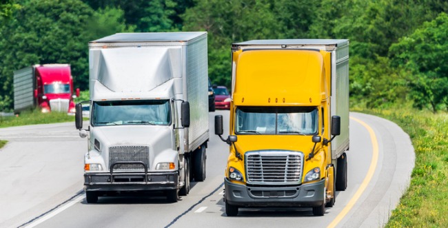 Two semi trucks driving side by side, one is white and one is yellow