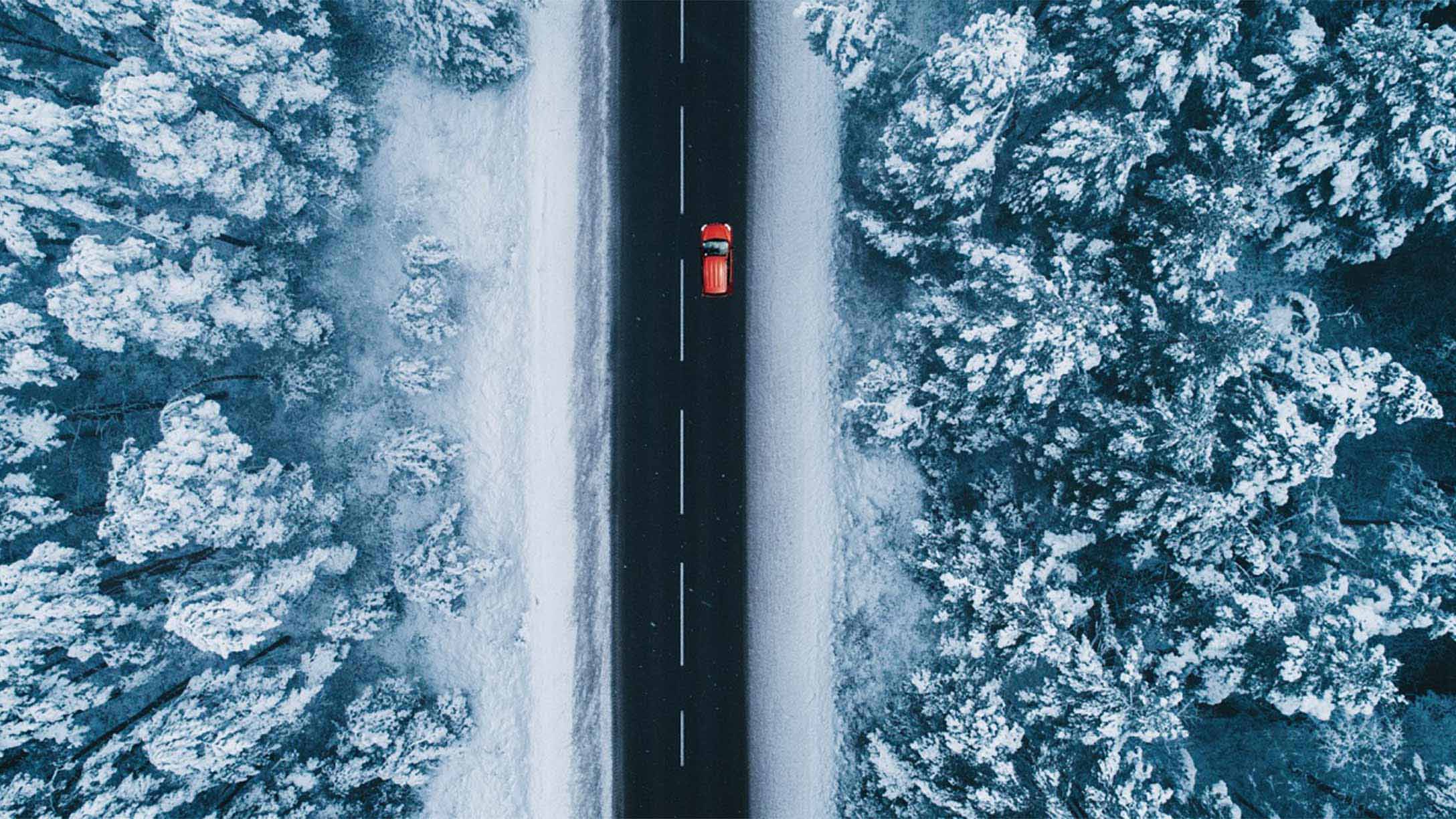 Ein Auto fährt auf einer Landstraße in einer Winterlandschaft.