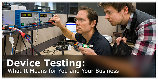 Two male employees at a desk with a unfinished GO device attached to wires for testing