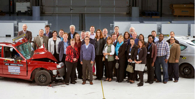 Image of a group of people standing next to a red car that was in an accident