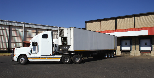 Large white transportation truck parked outside of shipping warehouse