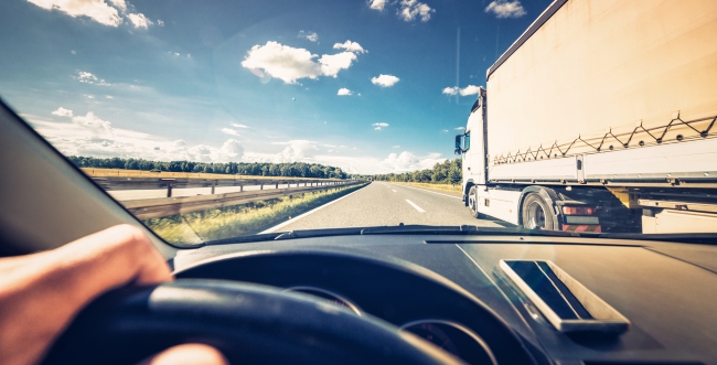 Point of view from a driver in a car on the road with a white transport truck in the right lane.