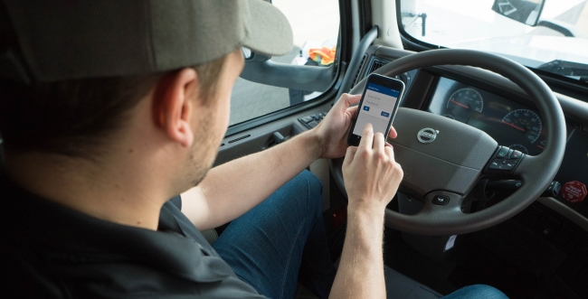 Male employee sitting behind steering wheel with phone in their hands