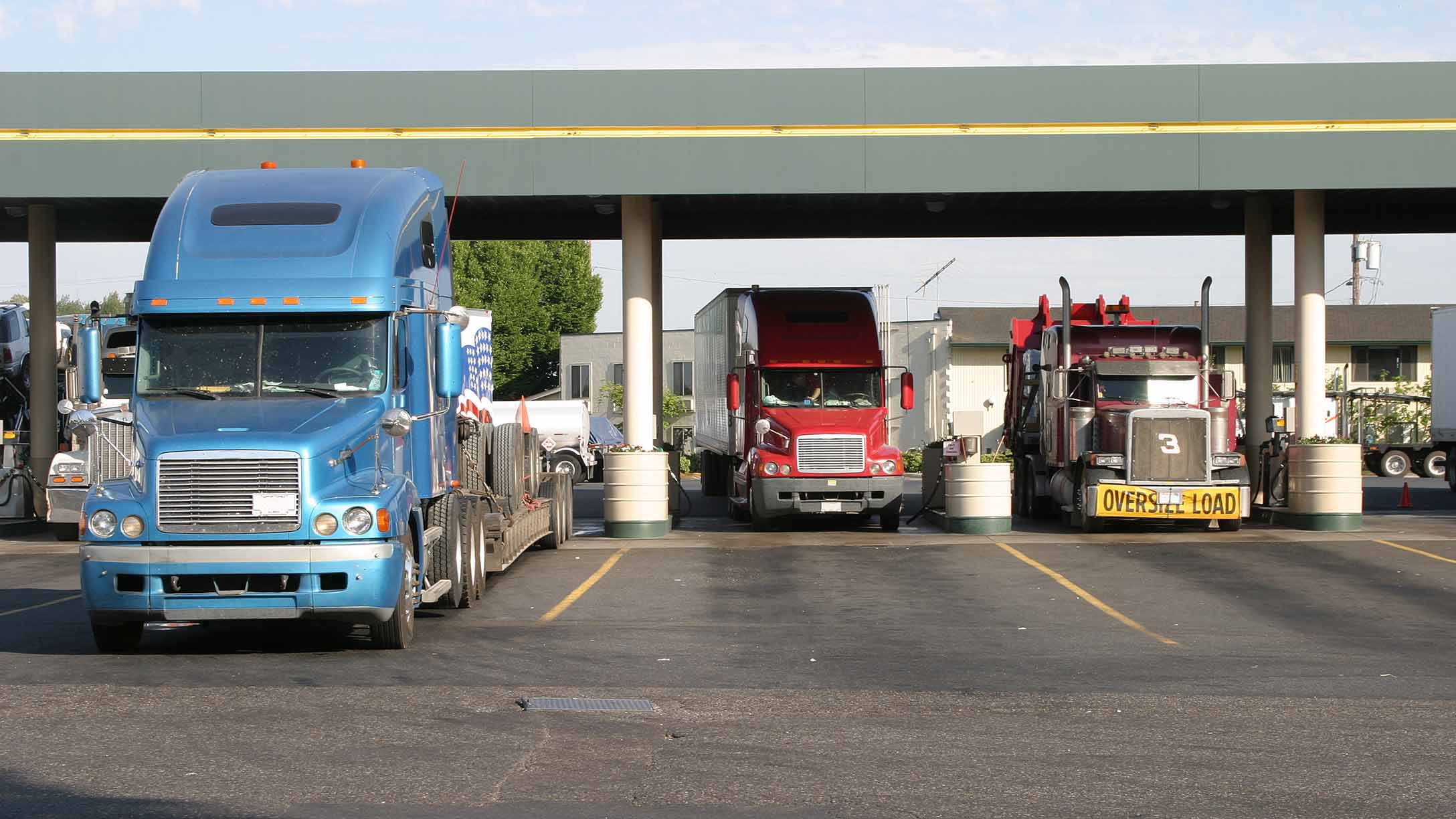 Three semi trucks filling up at a gas station