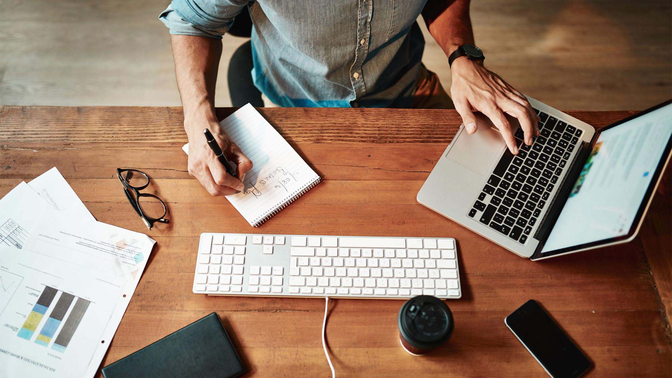 Person sitting at desk using a computer and writing in a notebook at the same time