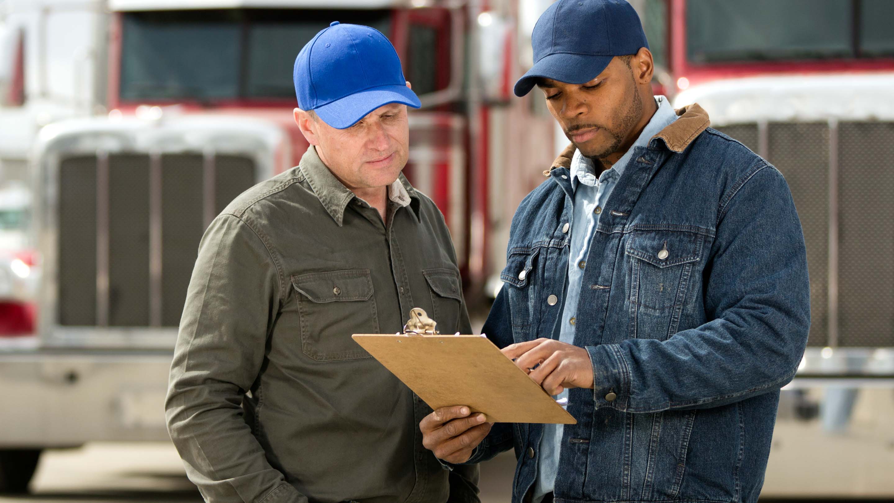 Two people looking at clipboard in front of two trucks