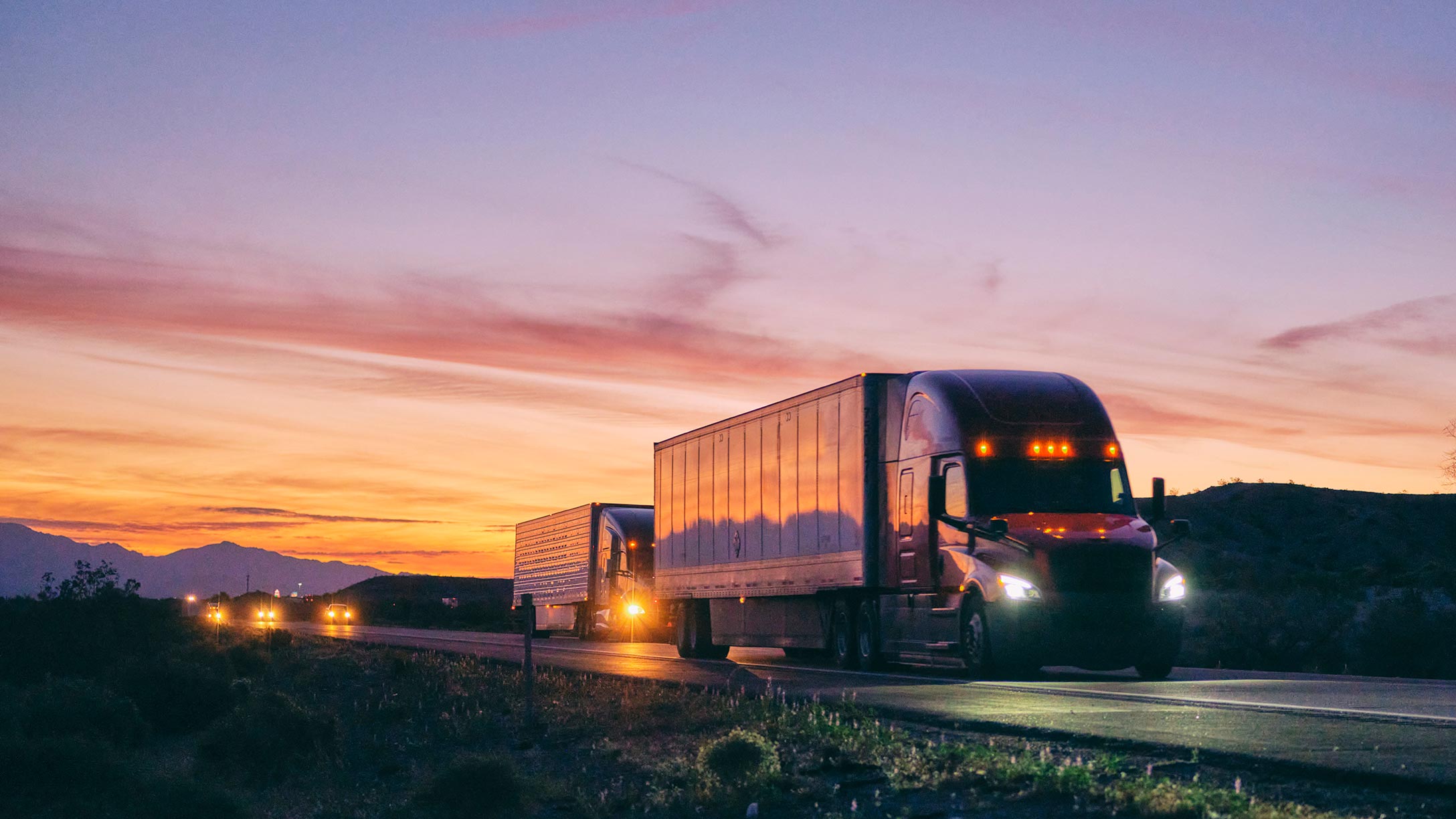 A truck driving on the highway with the evening sky behind