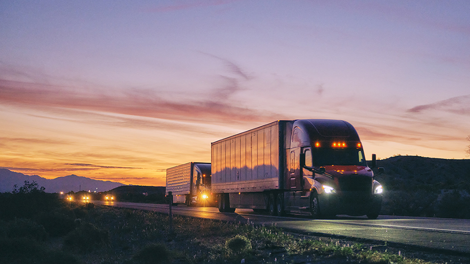 A truck driving on the highway with the evening sky behind