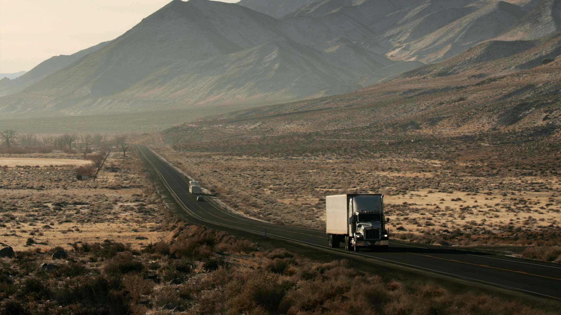 Truck driving on open road with mountains in the background