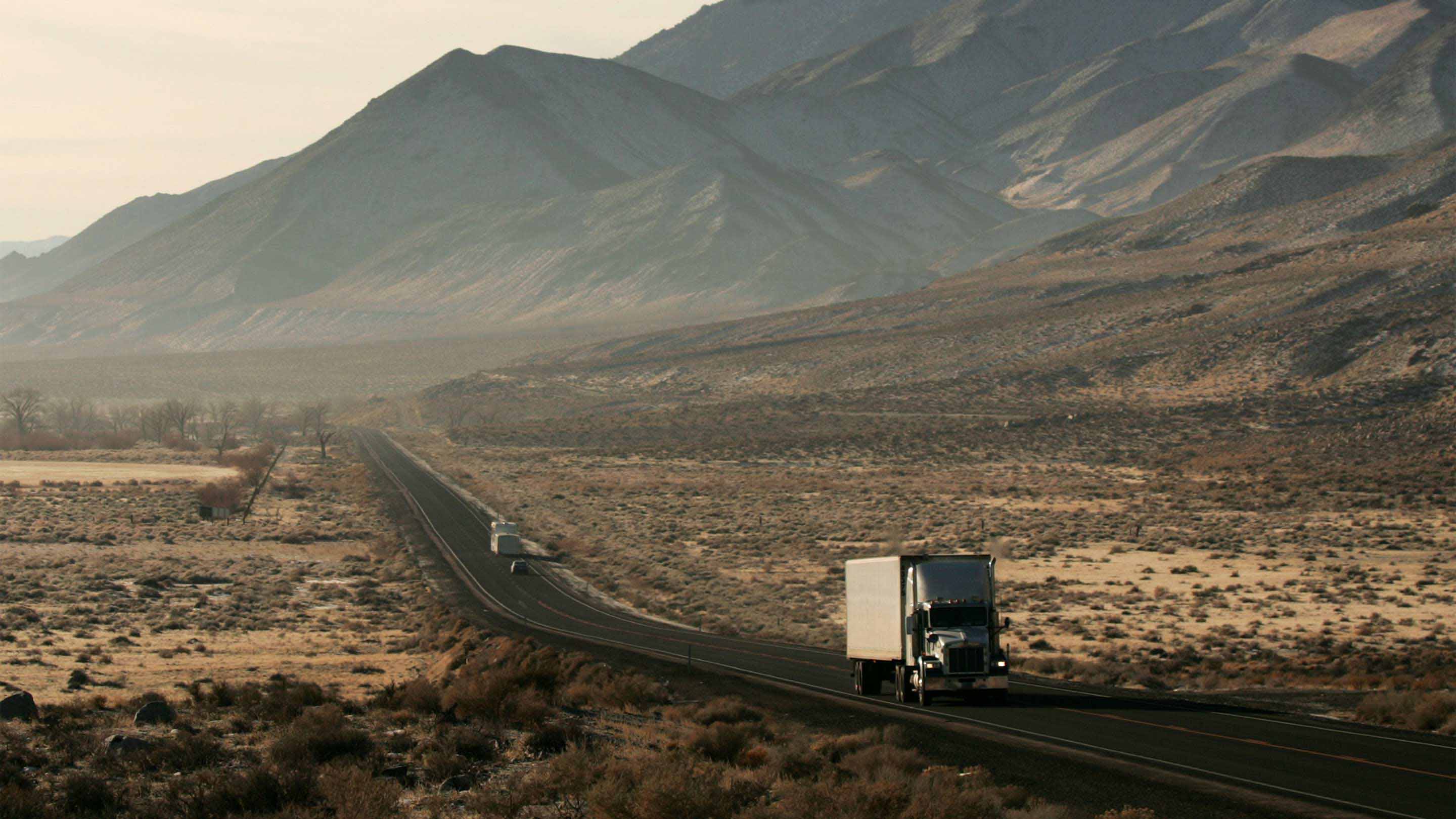 Truck driving on open road with mountains in the background