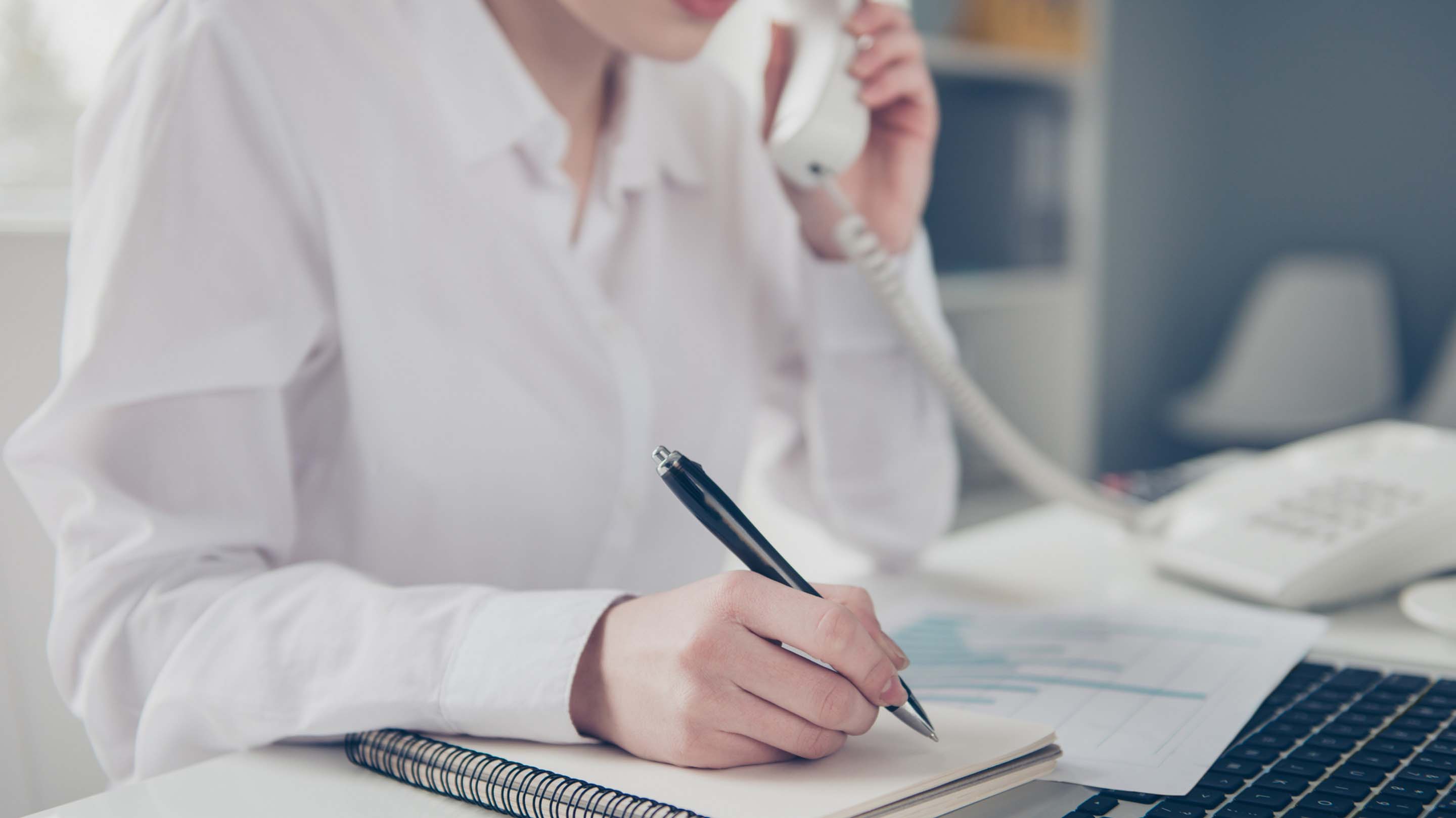 Person speaking on phone while writing something on paper