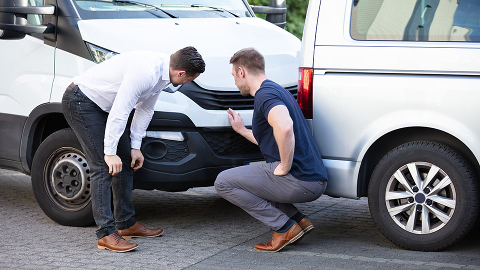 Two men at a vehicle collision looking at damage