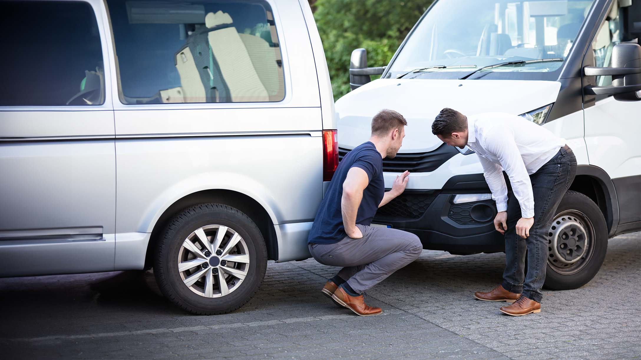 Two men at a vehicle collision looking at damage