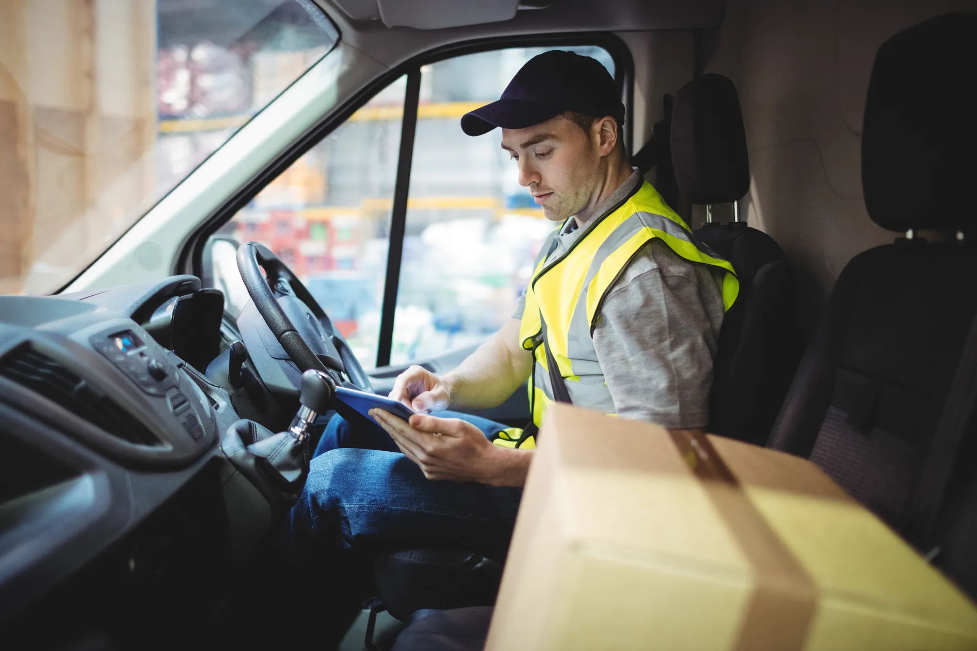 The image captures a moment in the working life of a delivery driver, using technology to manage delivery logistics. It highlights the integration of digital tools in the transportation and delivery sector.