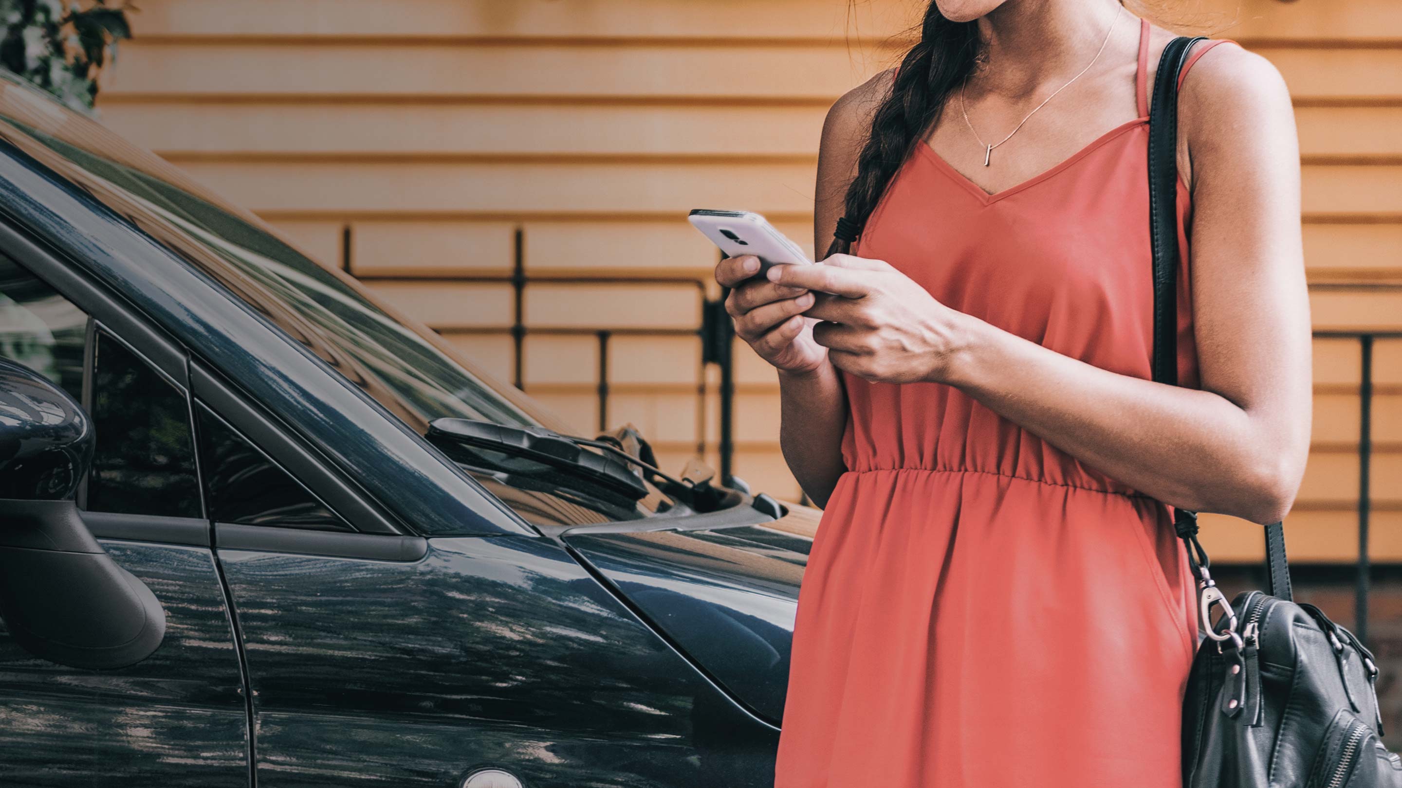 Persona de pie al lado de un coche sosteniendo y mirando un smartphone
