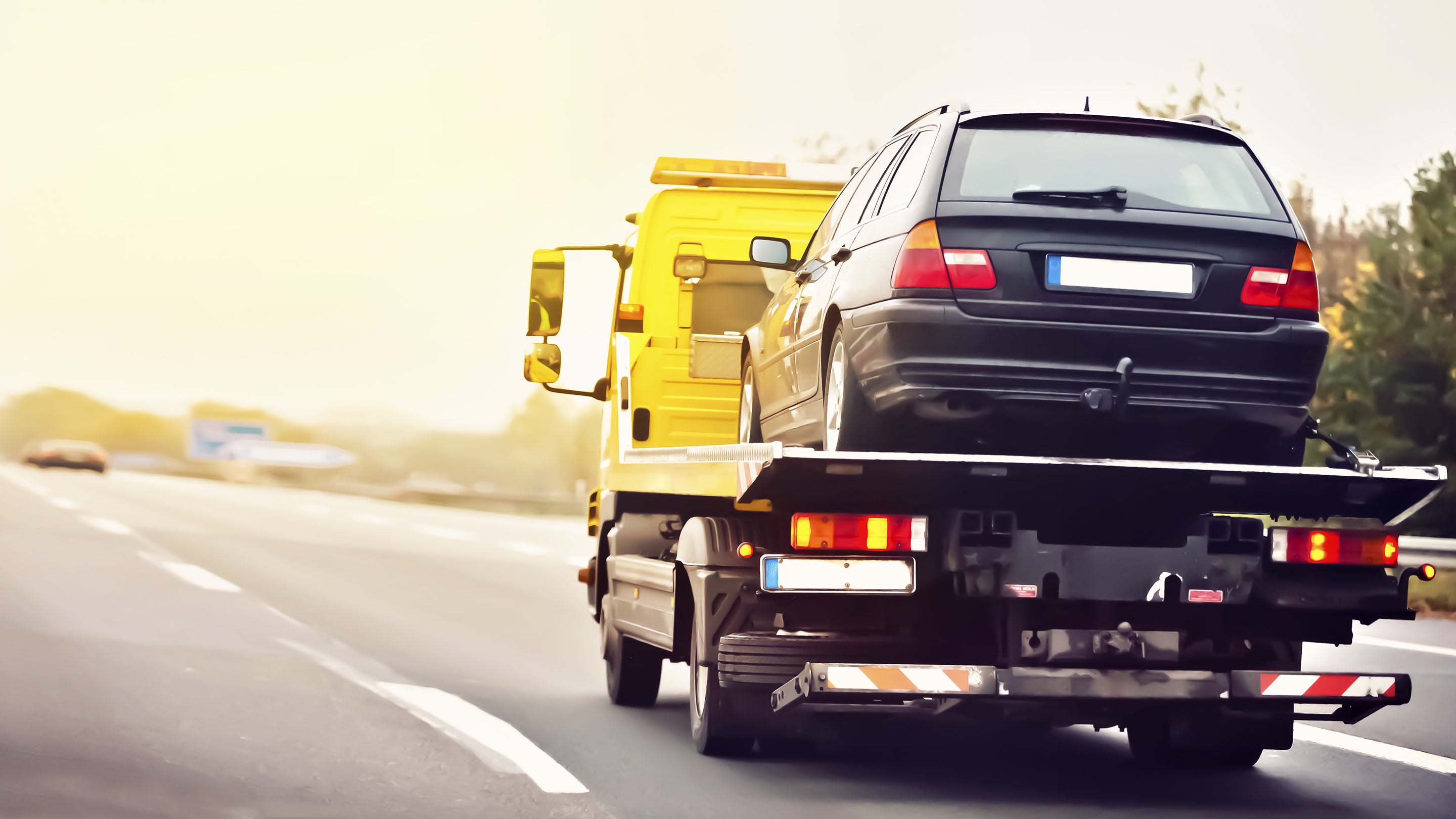 Ein Abschleppwagen fährt mit einem aufgeladenem Fahrzeug eine Straße entlang.