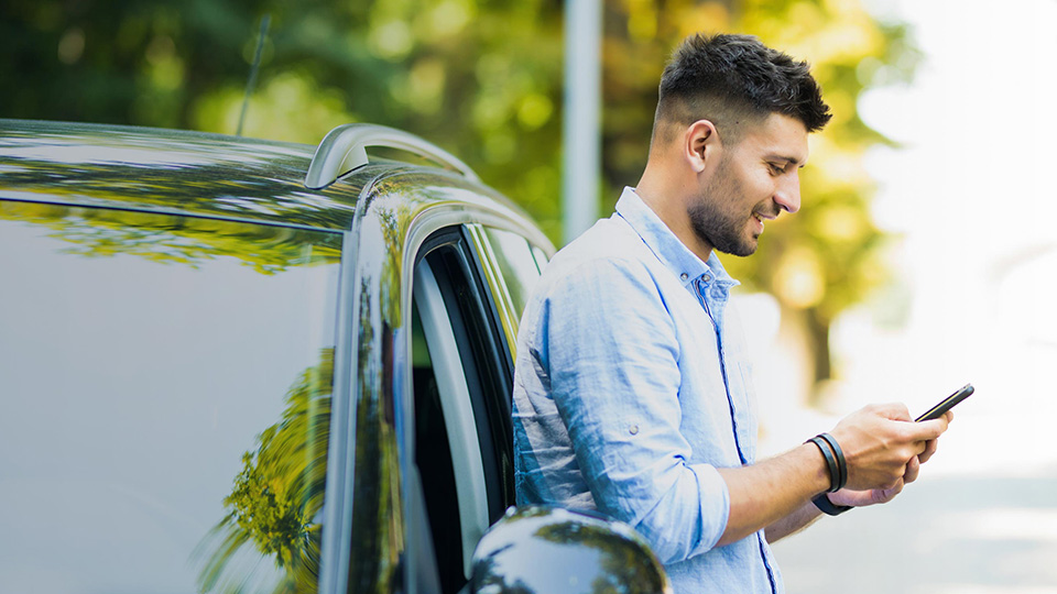 Mann an Auto angelehnt mit Handy in der Hand