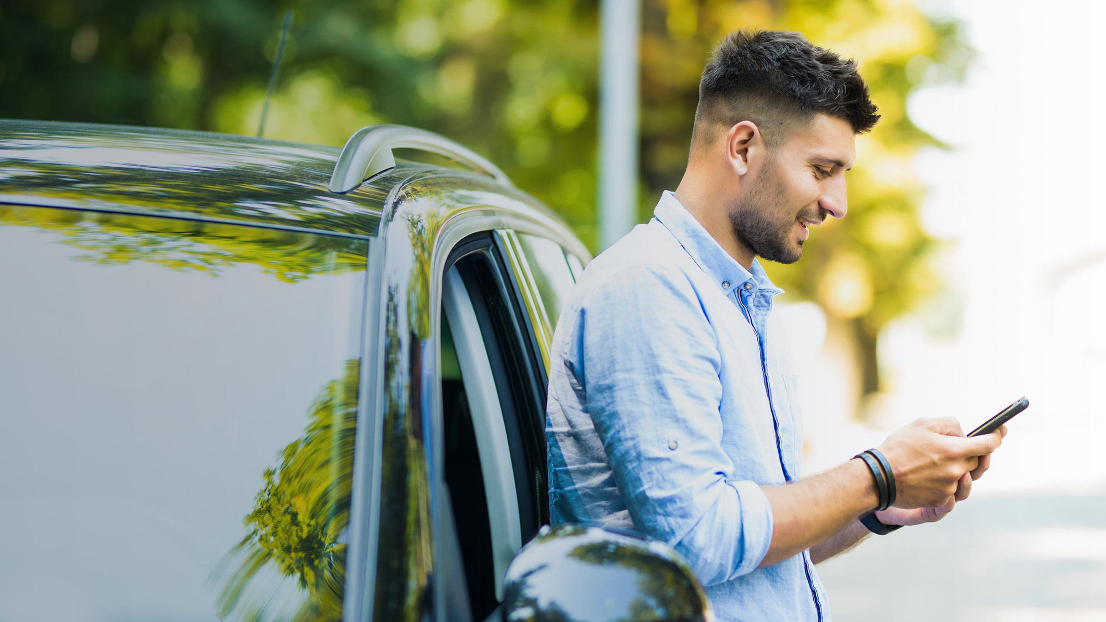 Mann an Auto angelehnt mit Handy in der Hand