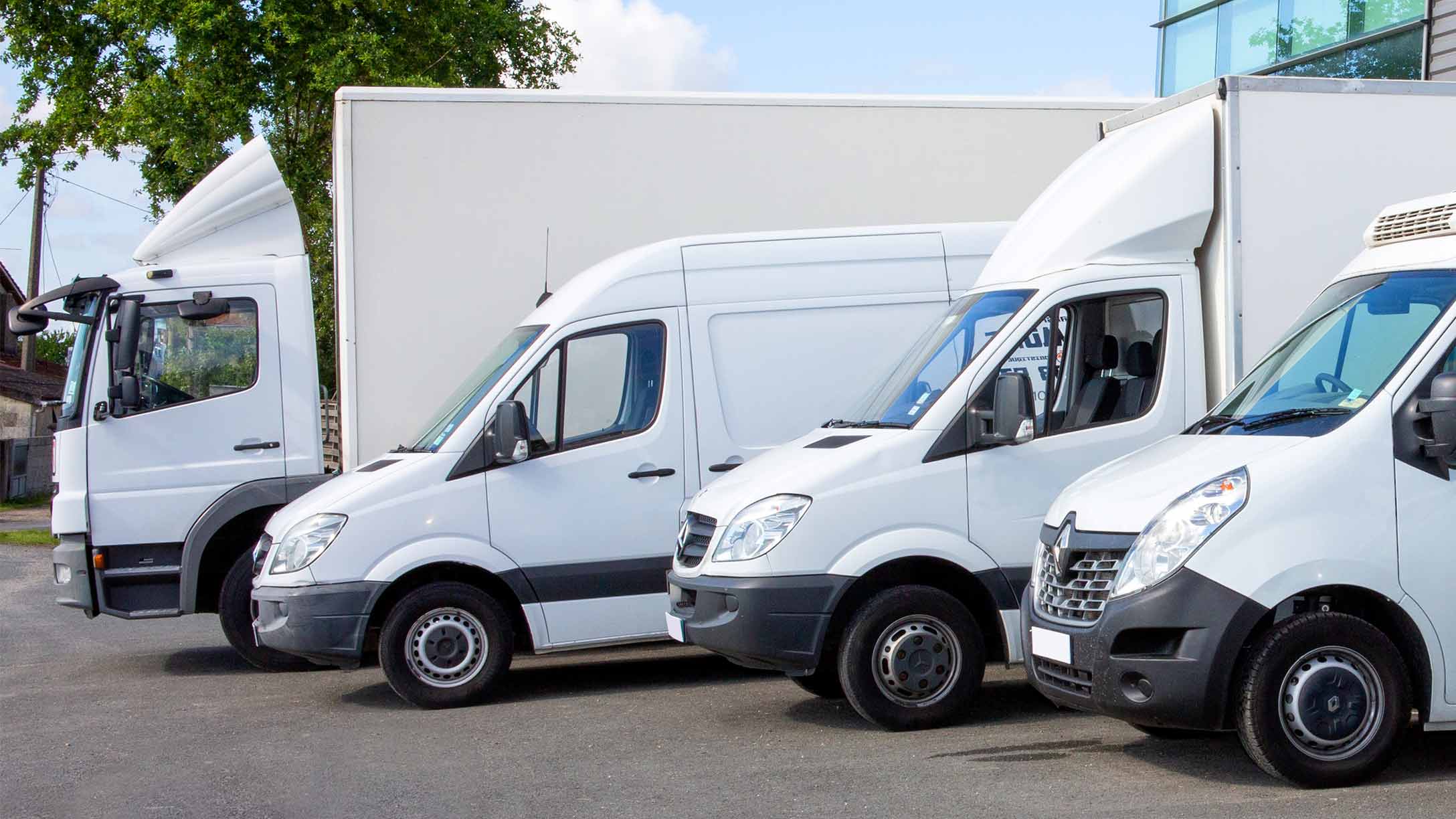 Mehrere weiße, nebeneinader geparkte Fahrzeuge, darunter ein kleiner Lkw und 3 Transporter.