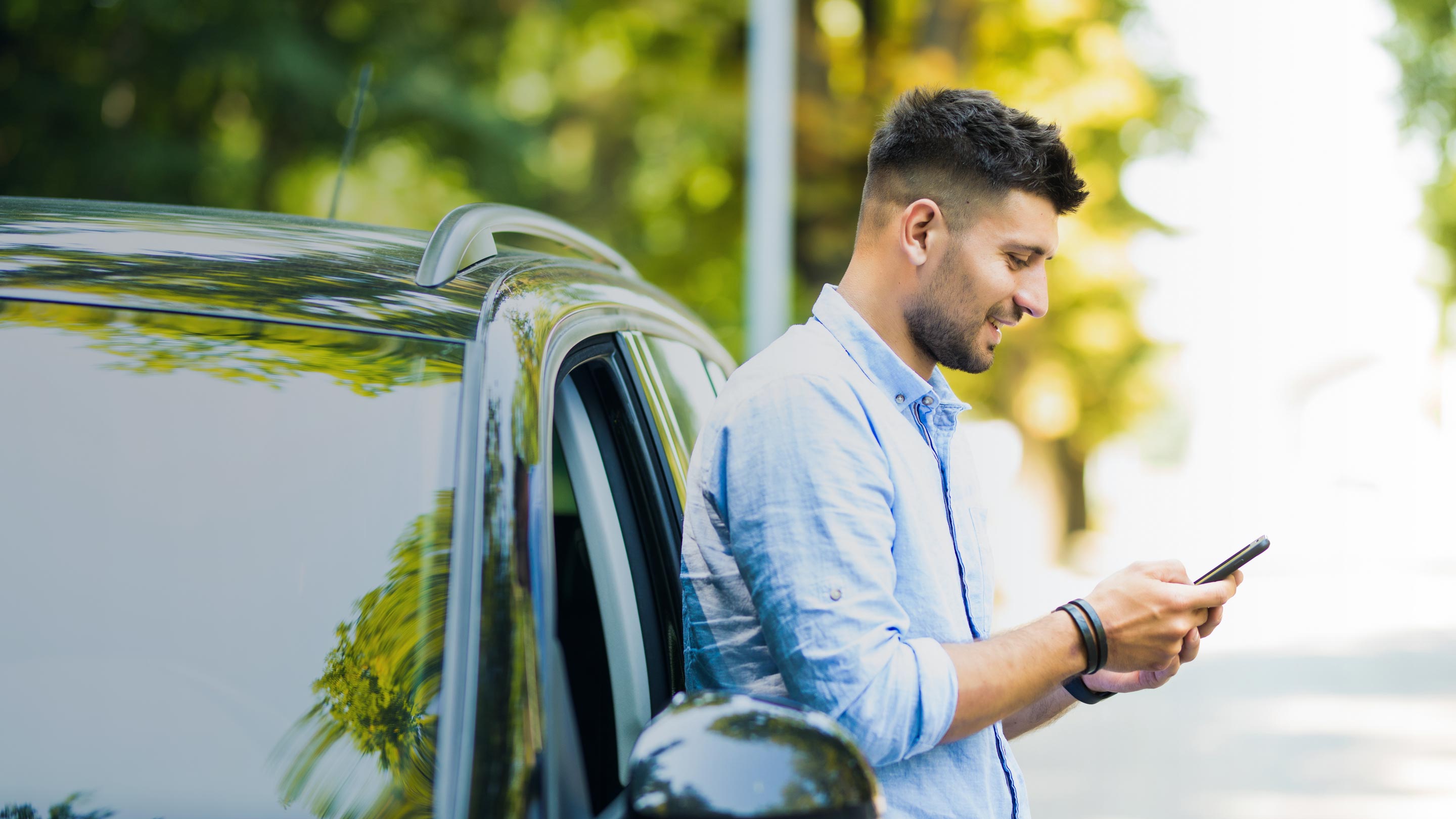 man leaning on car while using phone