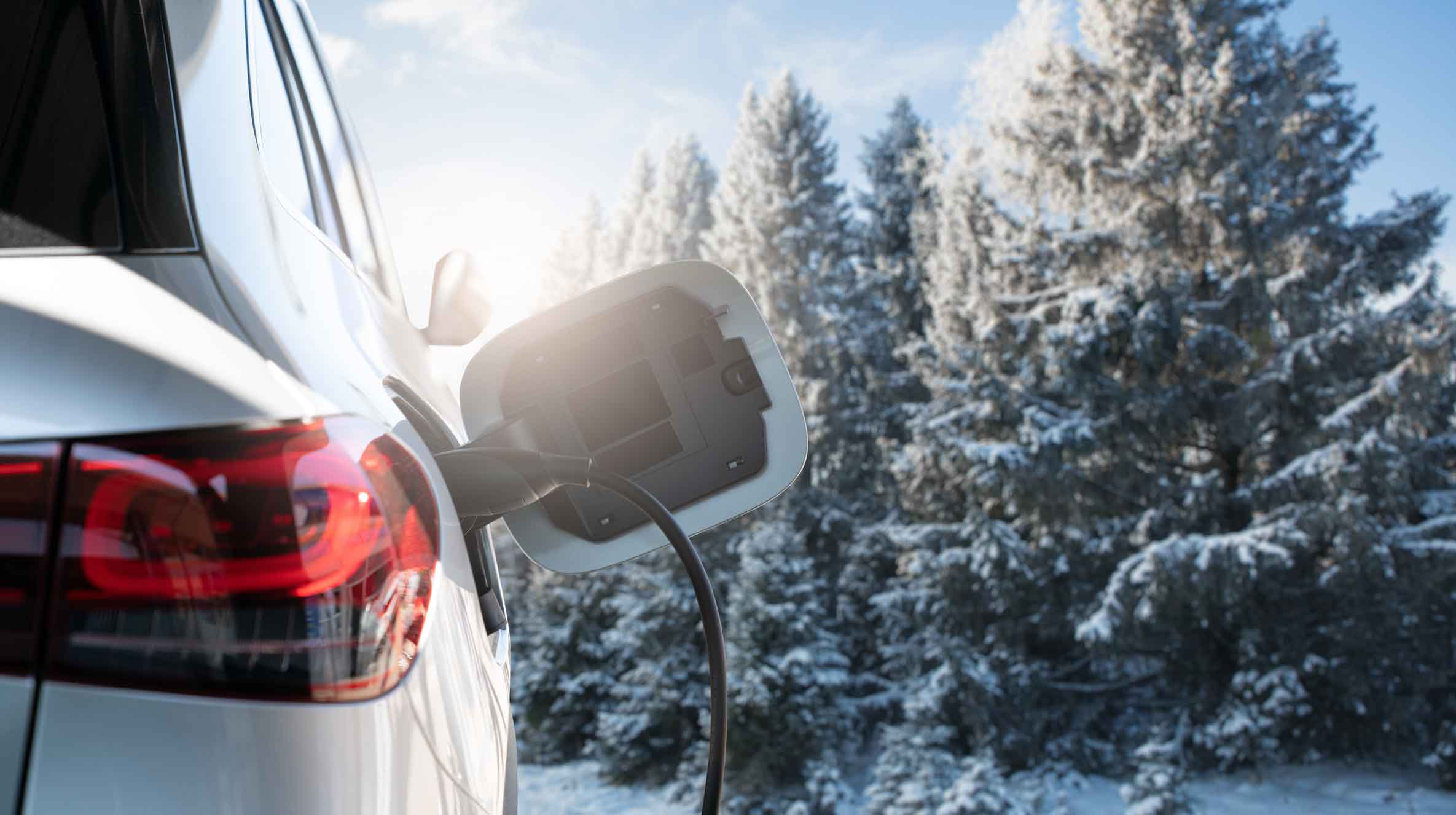 car charging in winter with trees in the background