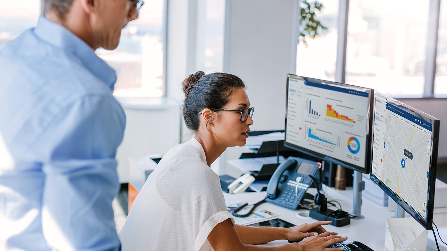 Mujer trabajando en dos monitores que muestran paneles de gráficos de MyGeotab